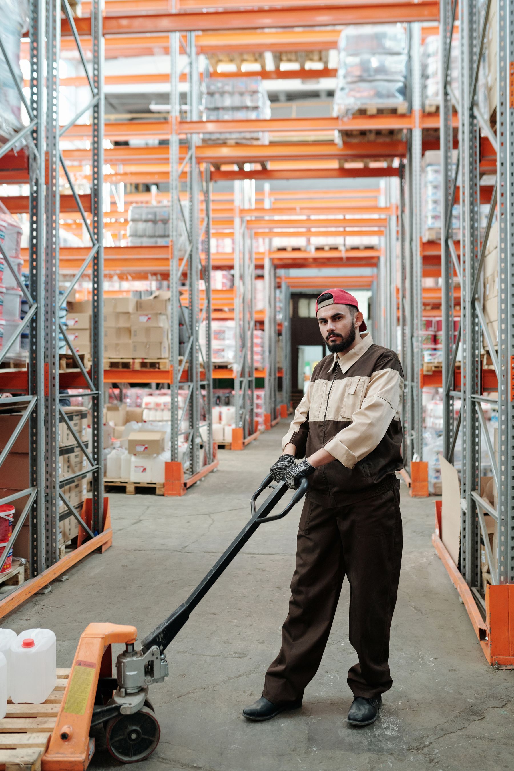Warehouse employee operating a hand pallet jack beside cartons and storage racks